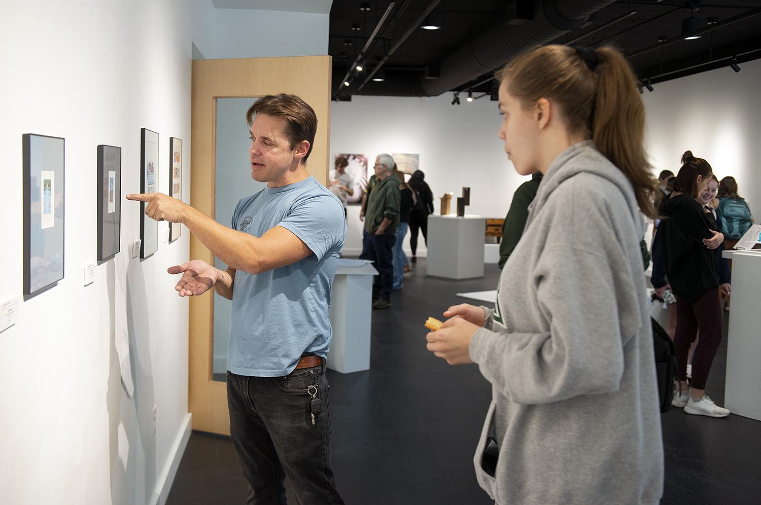 BSU faculty member pointing to art in a gallery and speaking with a student